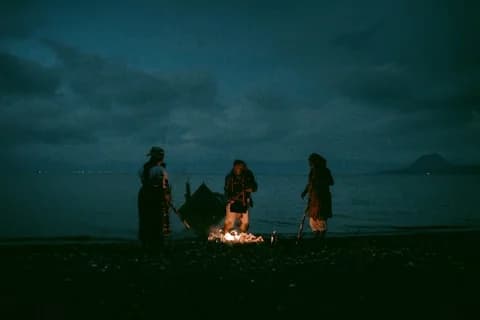 Three people around a beach campfire at dusk