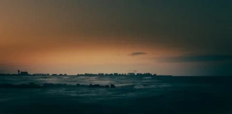 Distant city skyline across a dark sea at sunset