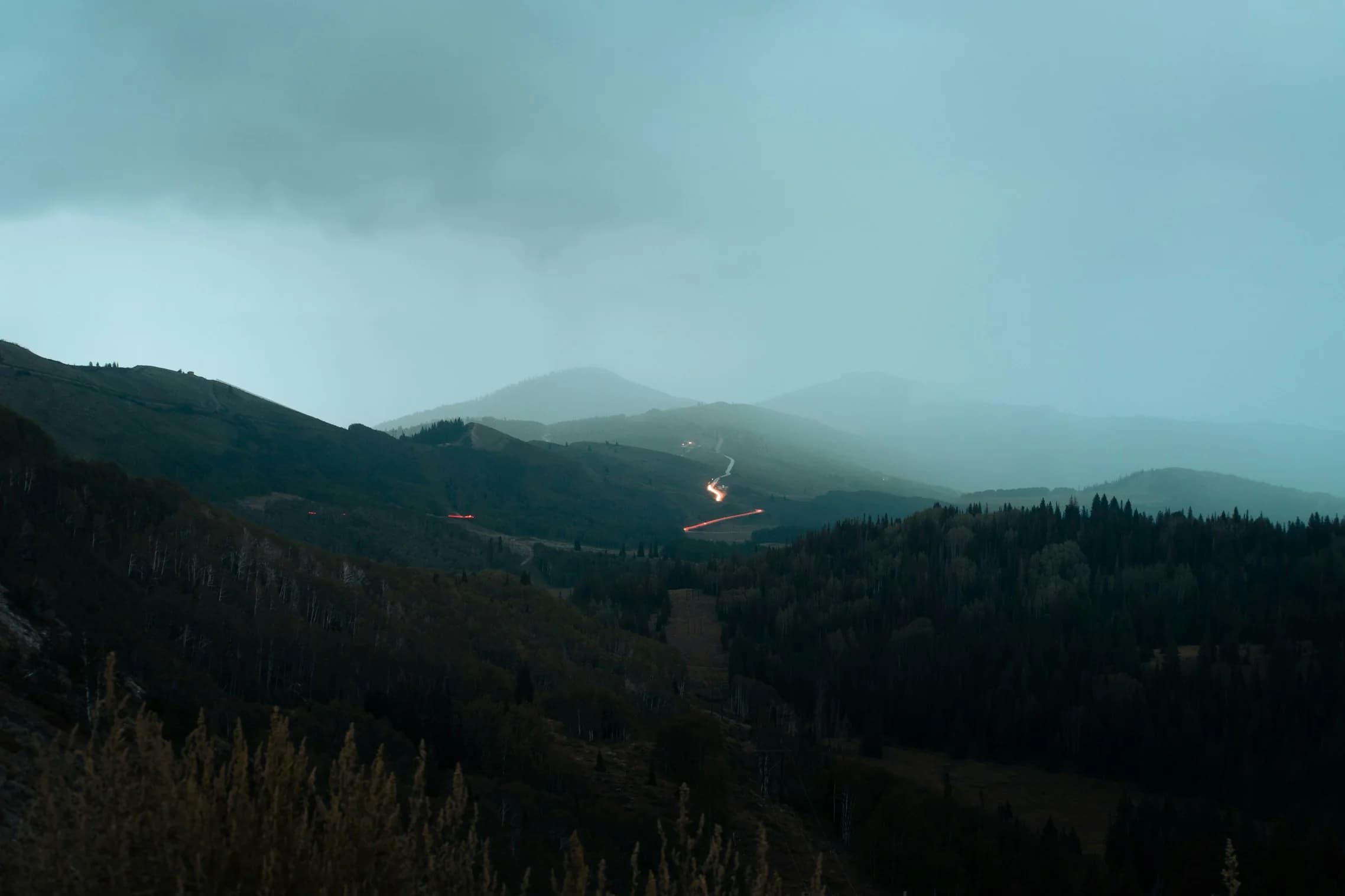 Misty mountain valley at dusk with winding car light trails